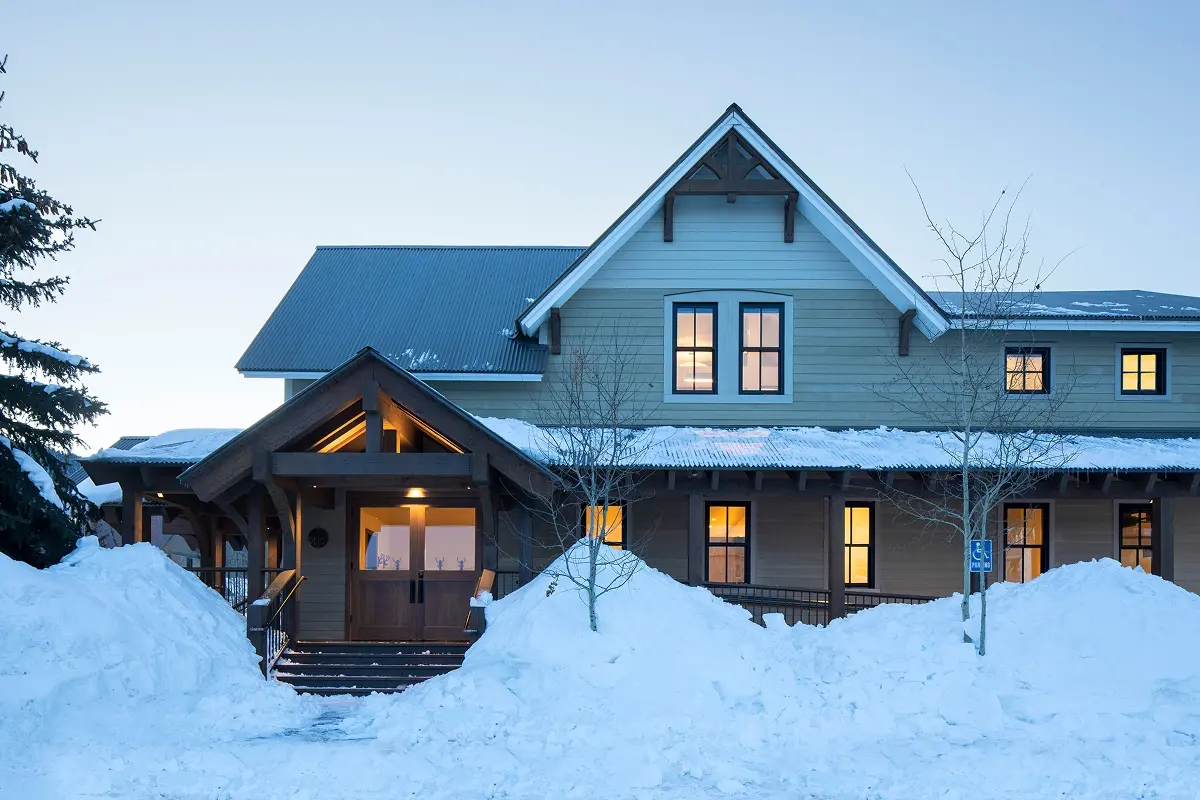 Warmly lit timber-framed entry at dusk, surrounded by snow at renovated community building.