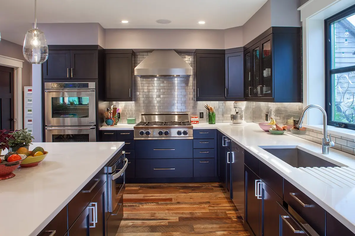 Custom kitchen design in Colorado featuring black cabinetry, reclaimed wood floors, stainless appliances, and a metallic tile backsplash.