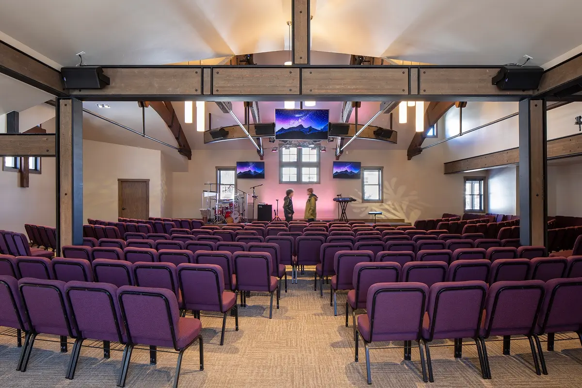 Interior sanctuary with glulam trusses, purple chairs, and multimedia screens for music and worship.