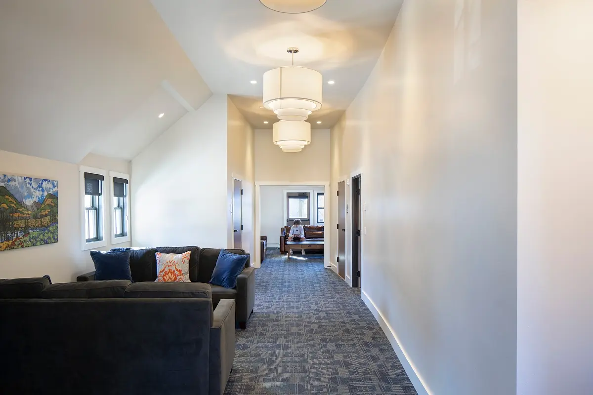 Upper-level hallway with blue carpet, lounge seating, and custom lighting for gathering.