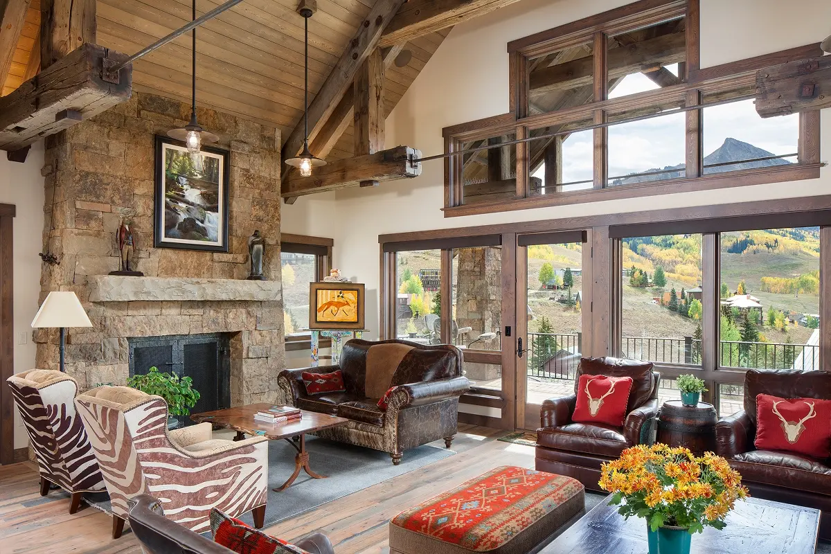 Warm mountain living room with stone fireplace, exposed beams, and window views of Mt. Crested Butte.