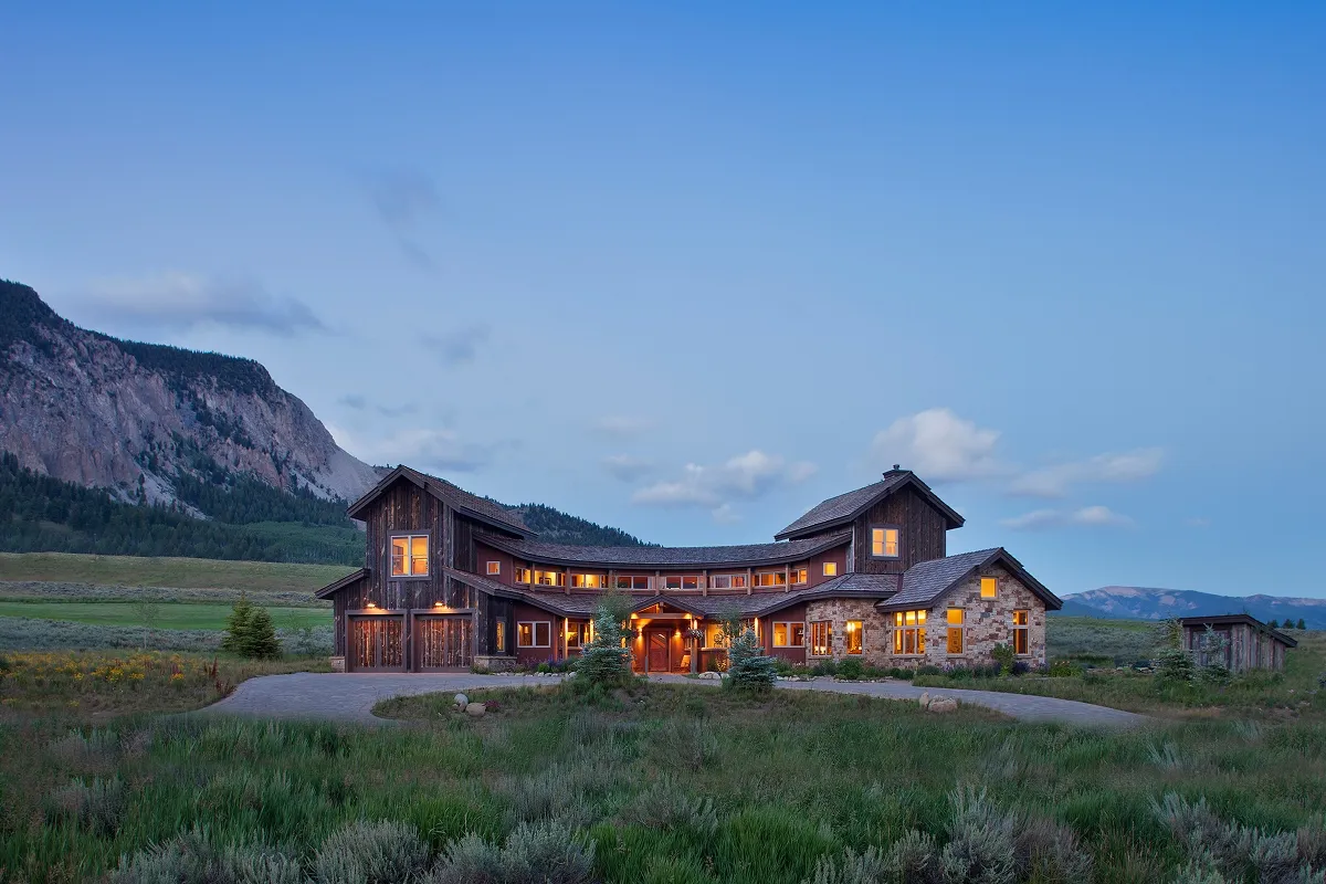 Symmetrical front view of curved mountain home with glowing interior windows and mountain backdrop.