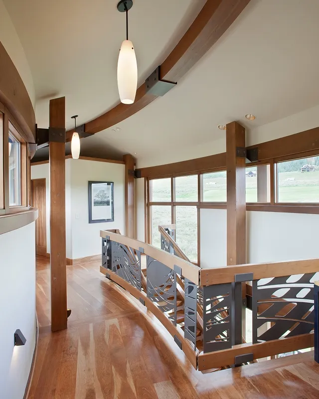 Curved upstairs hallway with wood beams, pendant lights, and expansive mountain-facing windows in Crested Butte home.