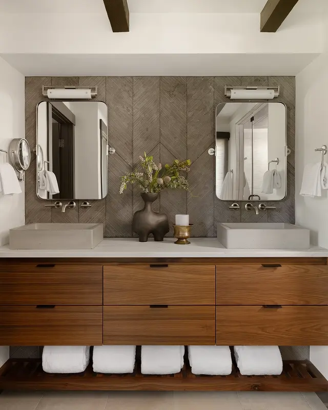 Bathroom renovation with double sink wood vanity, herringbone tile wall, and warm neutral tones.