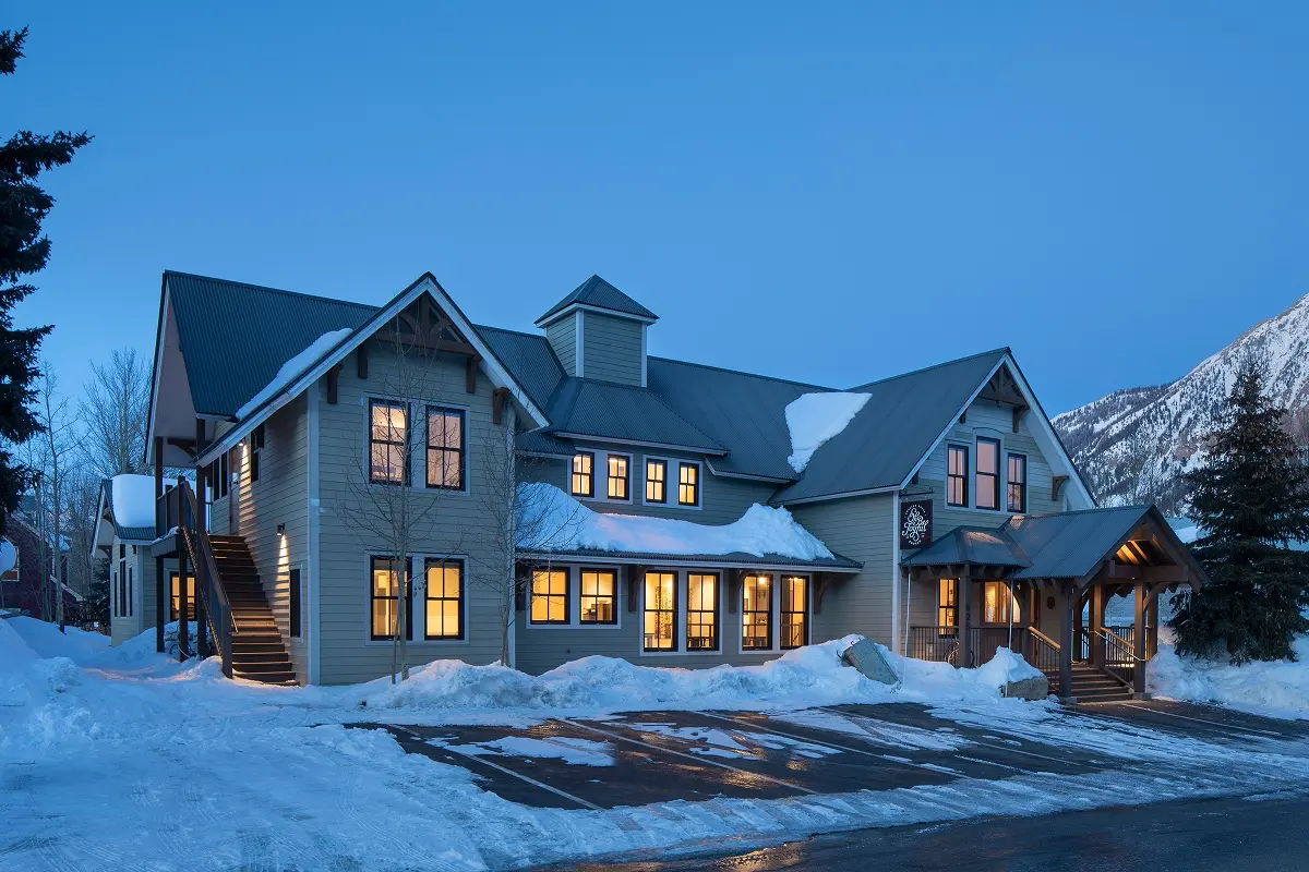 Snow-covered view of a renovated community building in downtown Crested Butte with warm interior lights glowing.