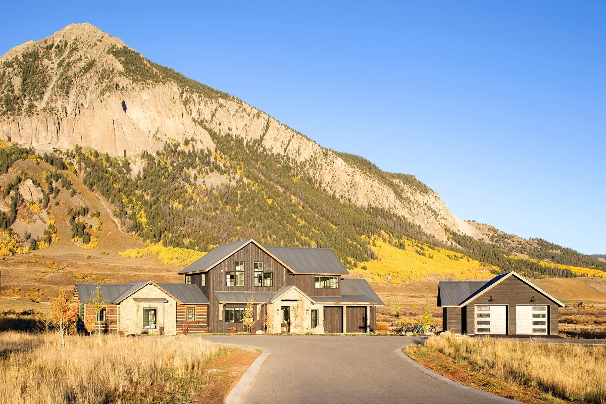 Modern mountain home in Crested Butte with dark siding and stone, surrounded by golden fall foliage.