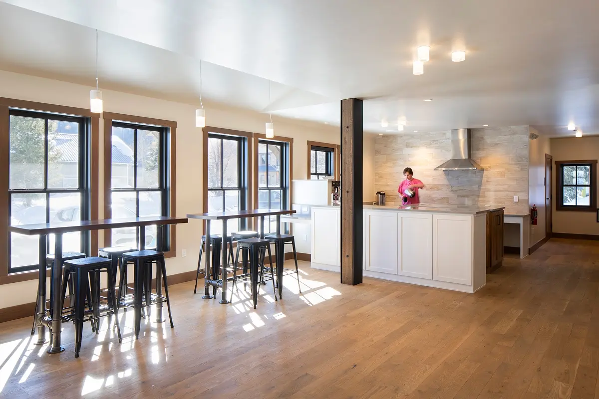 Bright, modern fellowship area with an open kitchen, white cabinetry, and tall windows.