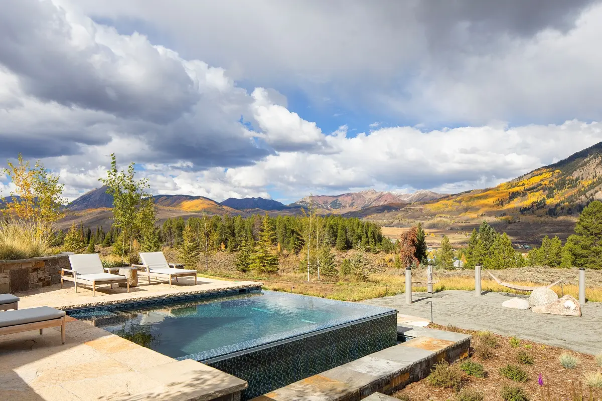 Heated infinity-edge pool surrounded by natural stone patio and modern loungers with mountain views.