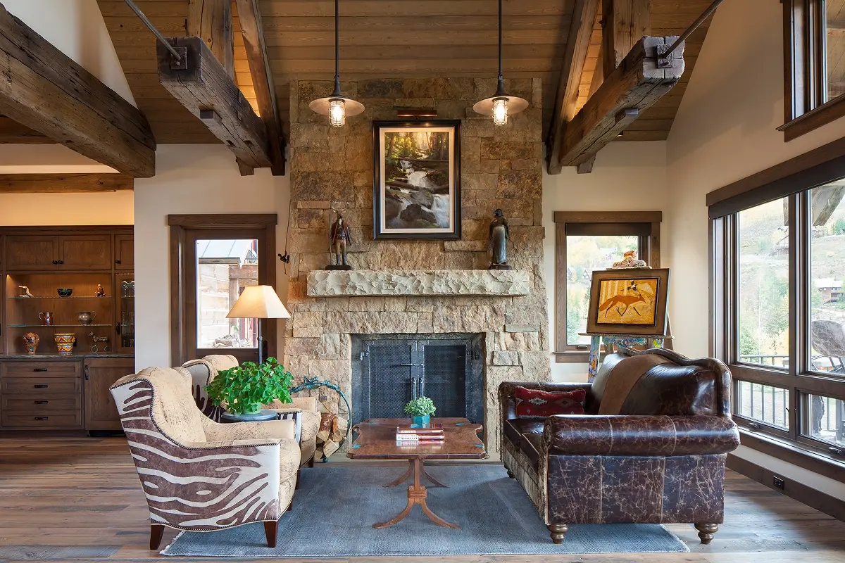 Warm mountain living room with stone fireplace, exposed beams, and window views of Mt. Crested Butte.