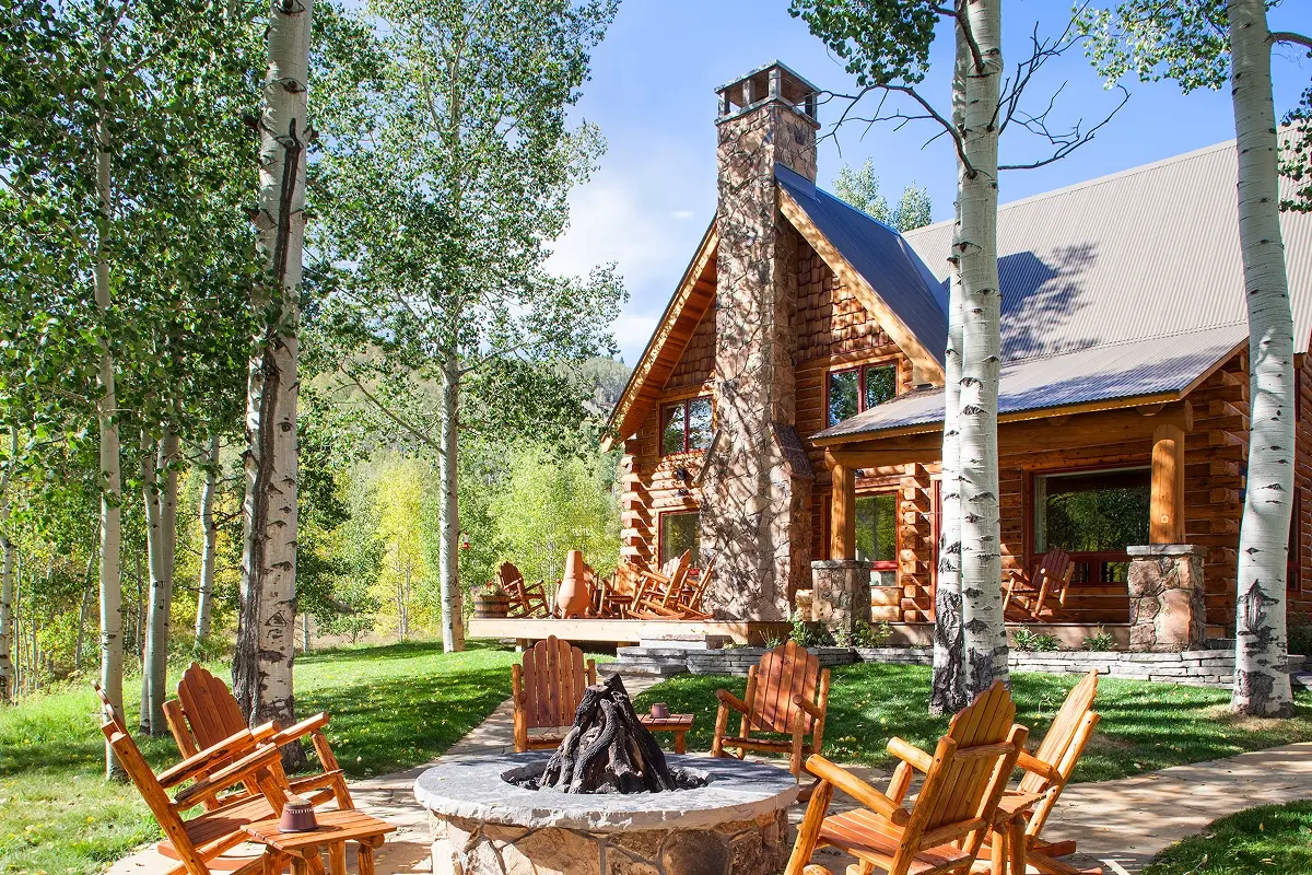 Rustic mountain home in Crested Butte with log siding and outdoor firepit beneath aspens.