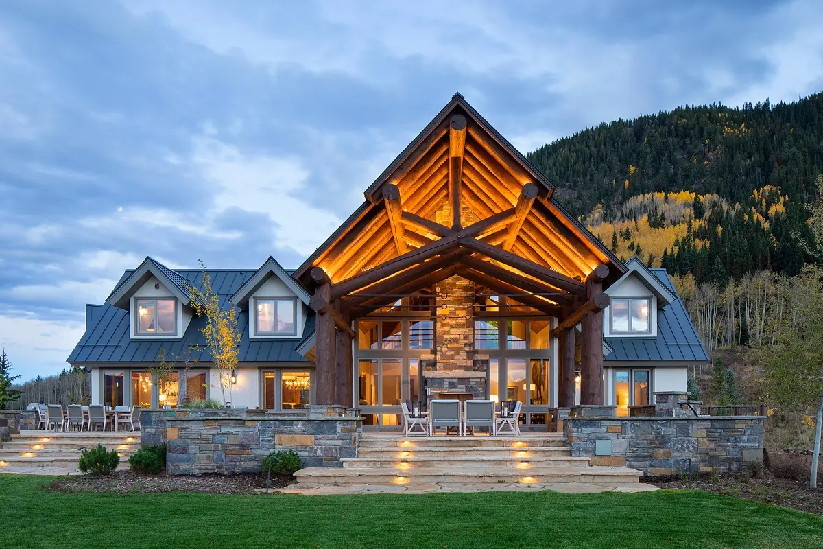 Evening view of log timber mountain home with glowing entry and large windows in Crested Butte.