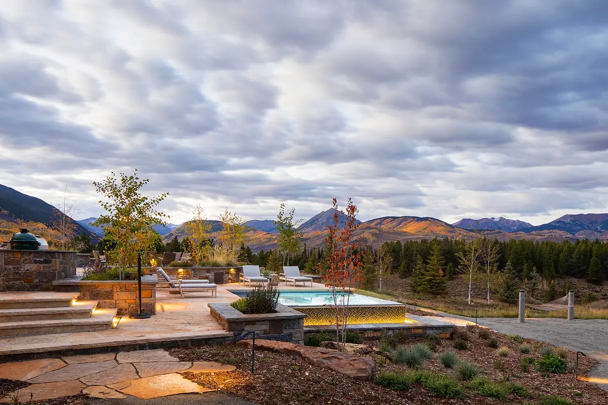 Multi-level flagstone patio and illuminated infinity-edge pool overlooking Crested Butte peaks at sunset.
