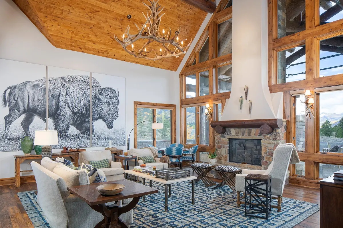 Vaulted mountain living room with wood ceilings, antler chandelier, and panoramic window views.