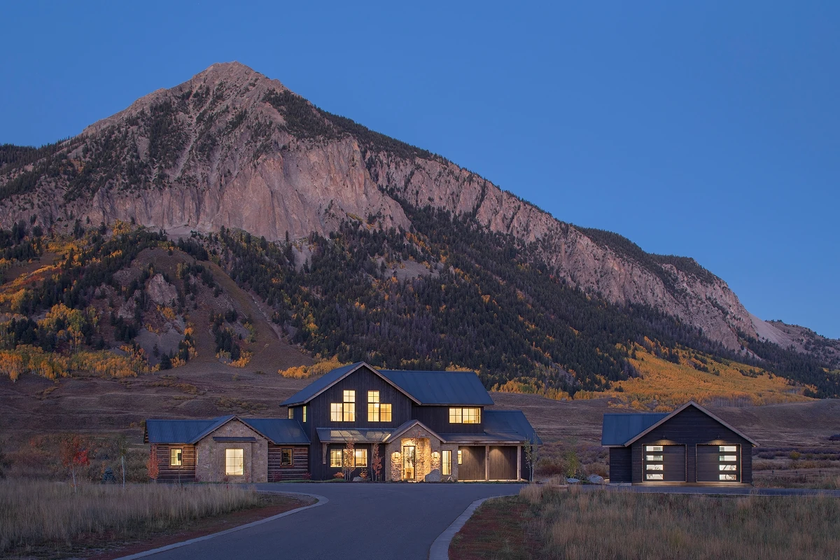 Nighttime view of a custom home in Aperture, Crested Butte with lit gables and a detached garage.