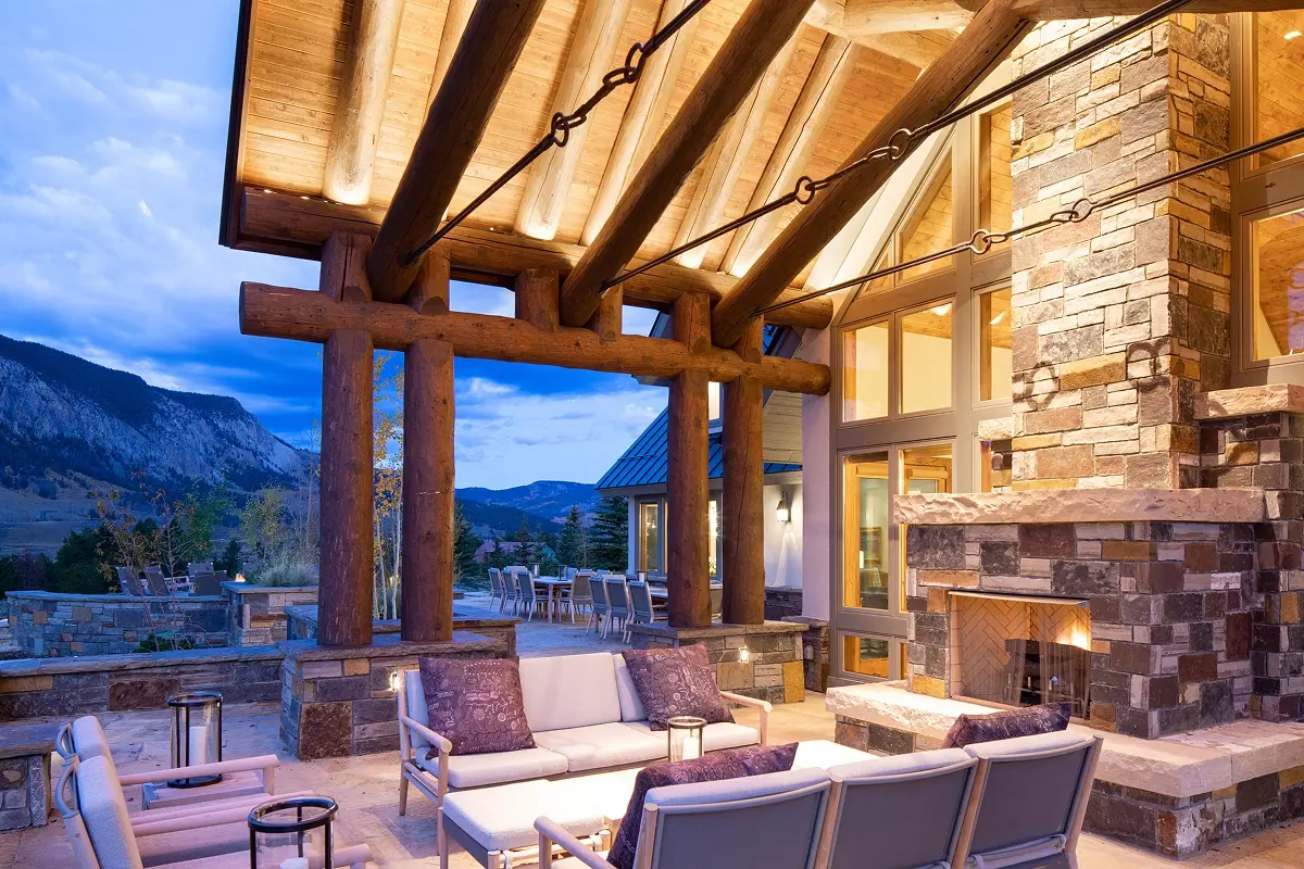 Outdoor fireplace surrounded by stone seating and timber beams, with mountain views beyond.