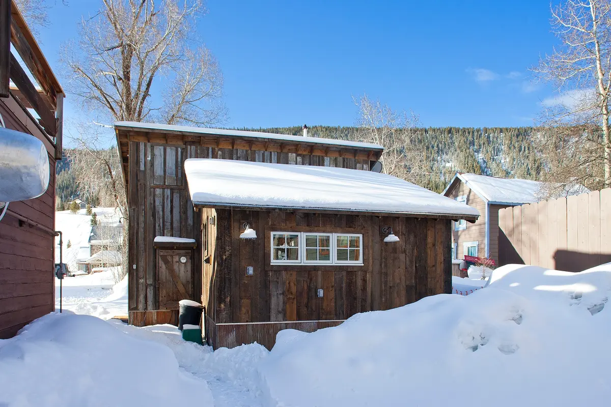 Side view of rustic Crested Butte studio rental framed by snow and alpine light.