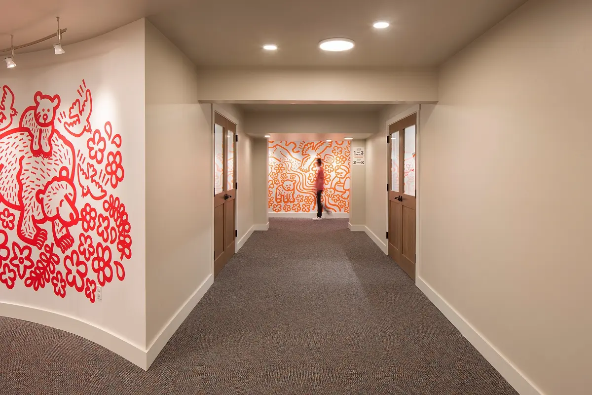 Daylit mural-covered hallway connecting updated youth classrooms in community space.