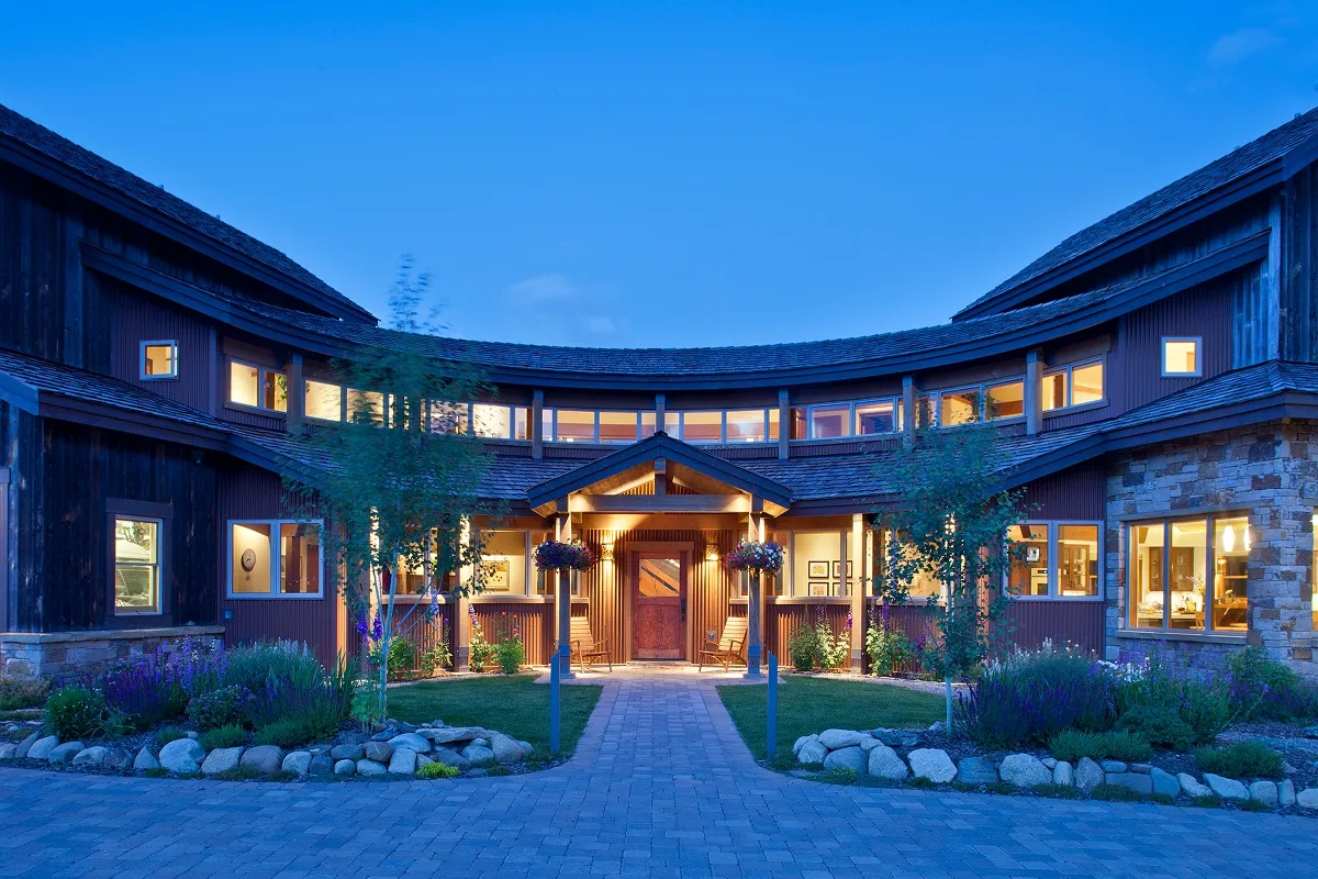 Close view of curved entryway with clerestory windows, stone and wood siding, and lush landscaping.