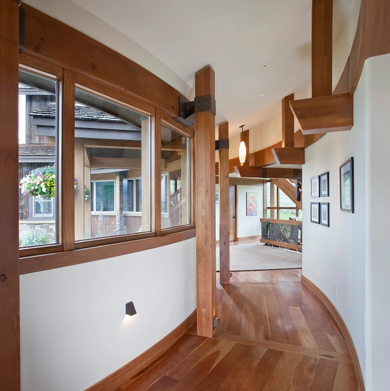 Curved hallway with exposed wood beams, warm wood flooring, and clerestory windows in a mountain home.