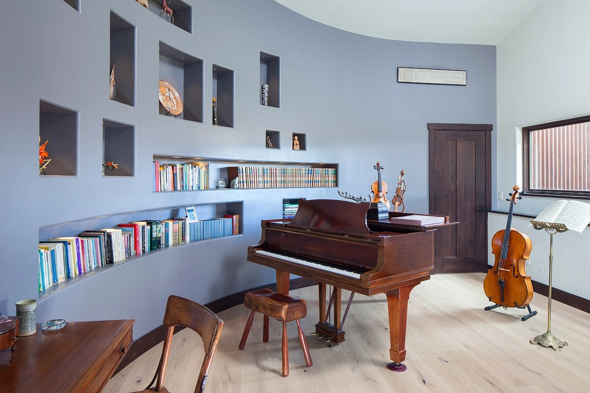 Music room with custom curved bookshelf wall and grand piano designed for acoustic resonance and display.