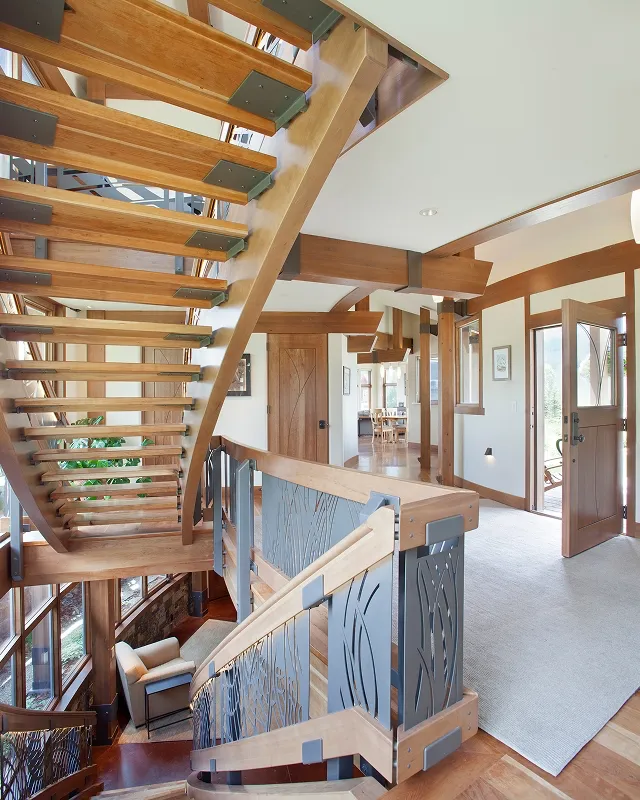 Multi-story curved floating staircase featuring cherry wood treads and steel railing with cutout designs.