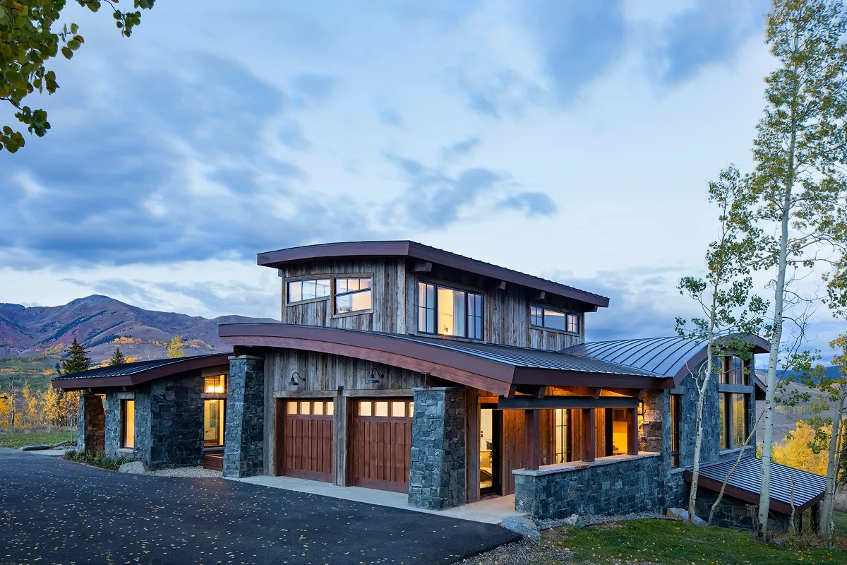 Garage side exterior of Surround House at twilight with rustic siding and metal roof.