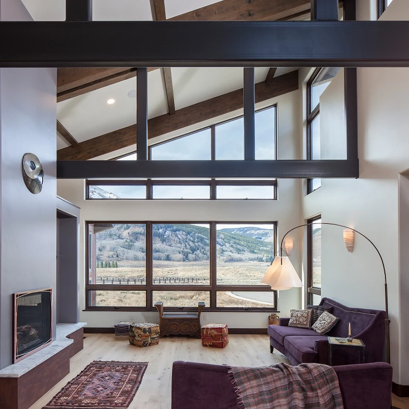 Great room with exposed steel trusses and panoramic windows overlooking the Crested Butte mountain landscape.
