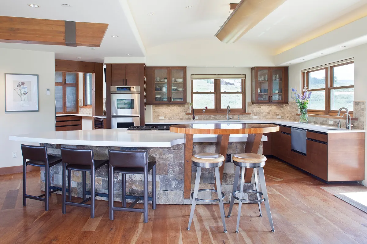 Bright kitchen interior with dual-height island, light wood flooring, and large mountain-facing windows.