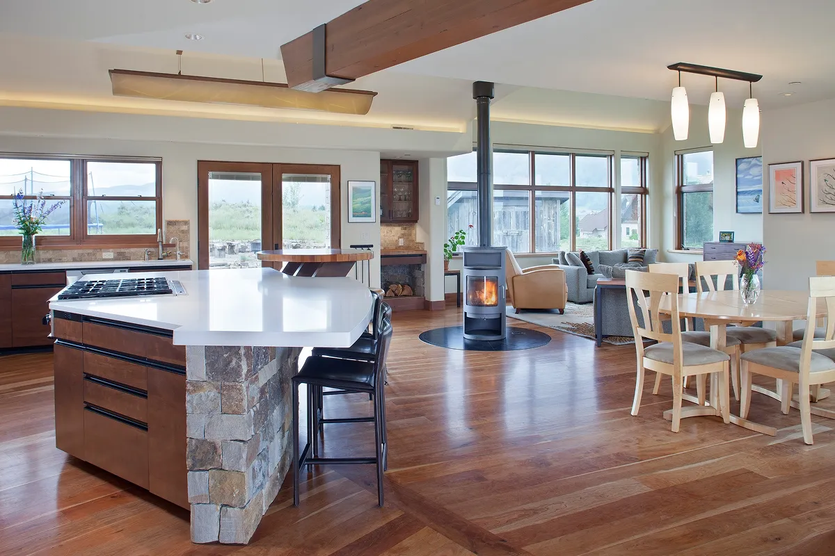 Spacious open-concept kitchen and dining area with geometric island, wood accents, and wood stove centerpiece.