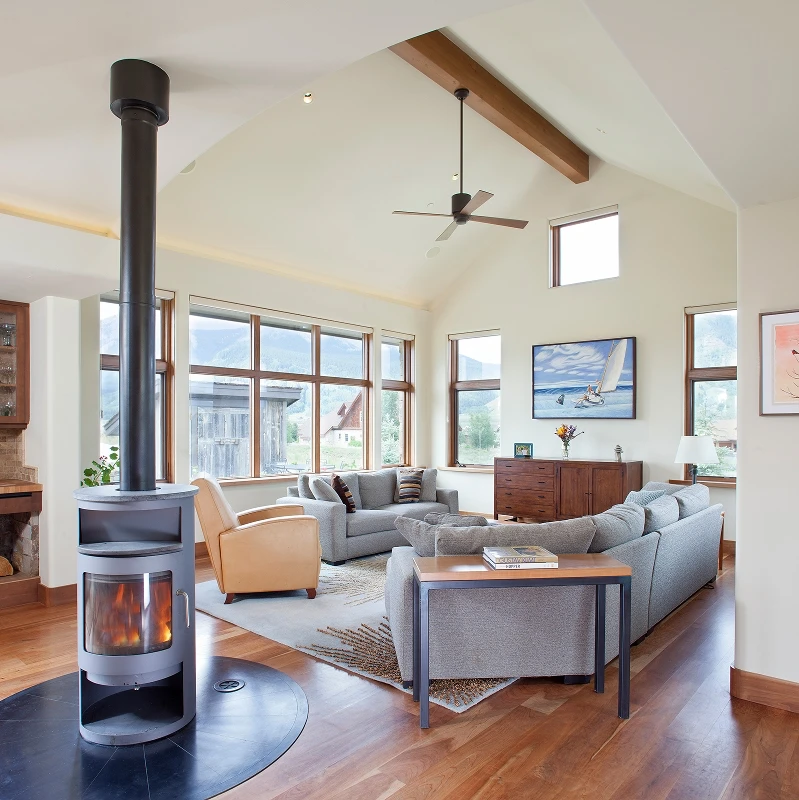 Alternate angle of modern living room featuring a wood stove, leather and gray seating, and exposed beam ceiling.