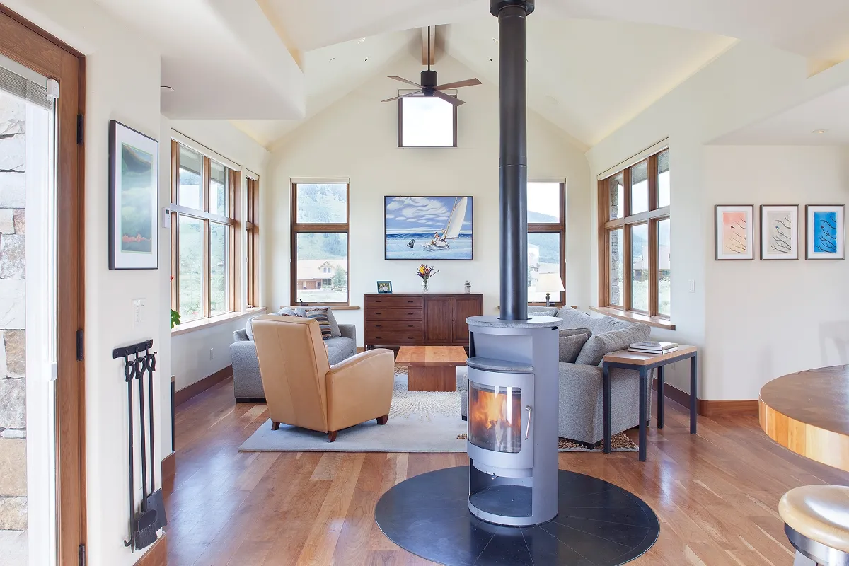 Contemporary living room with central wood stove, vaulted ceiling, and expansive mountain views through large windows.