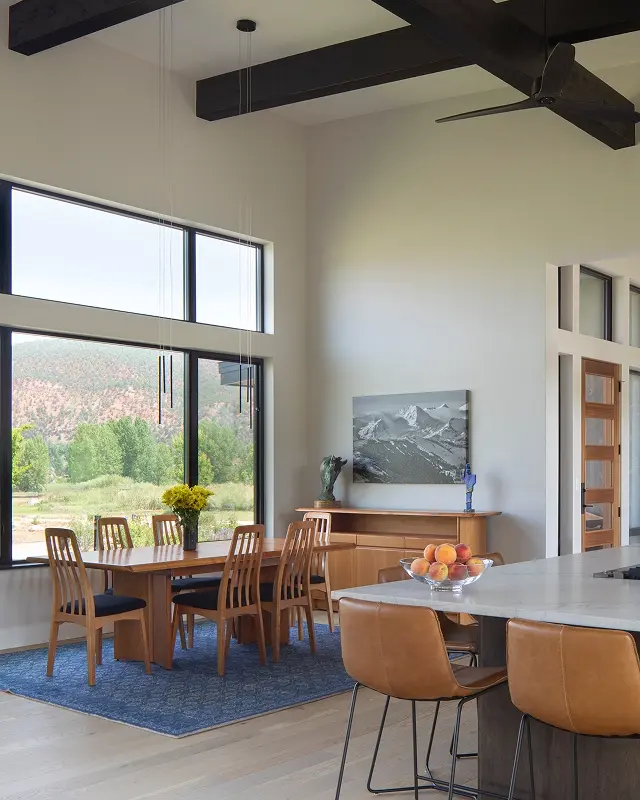 Luxury dining room with mountain views, black ceiling beams, and natural light.