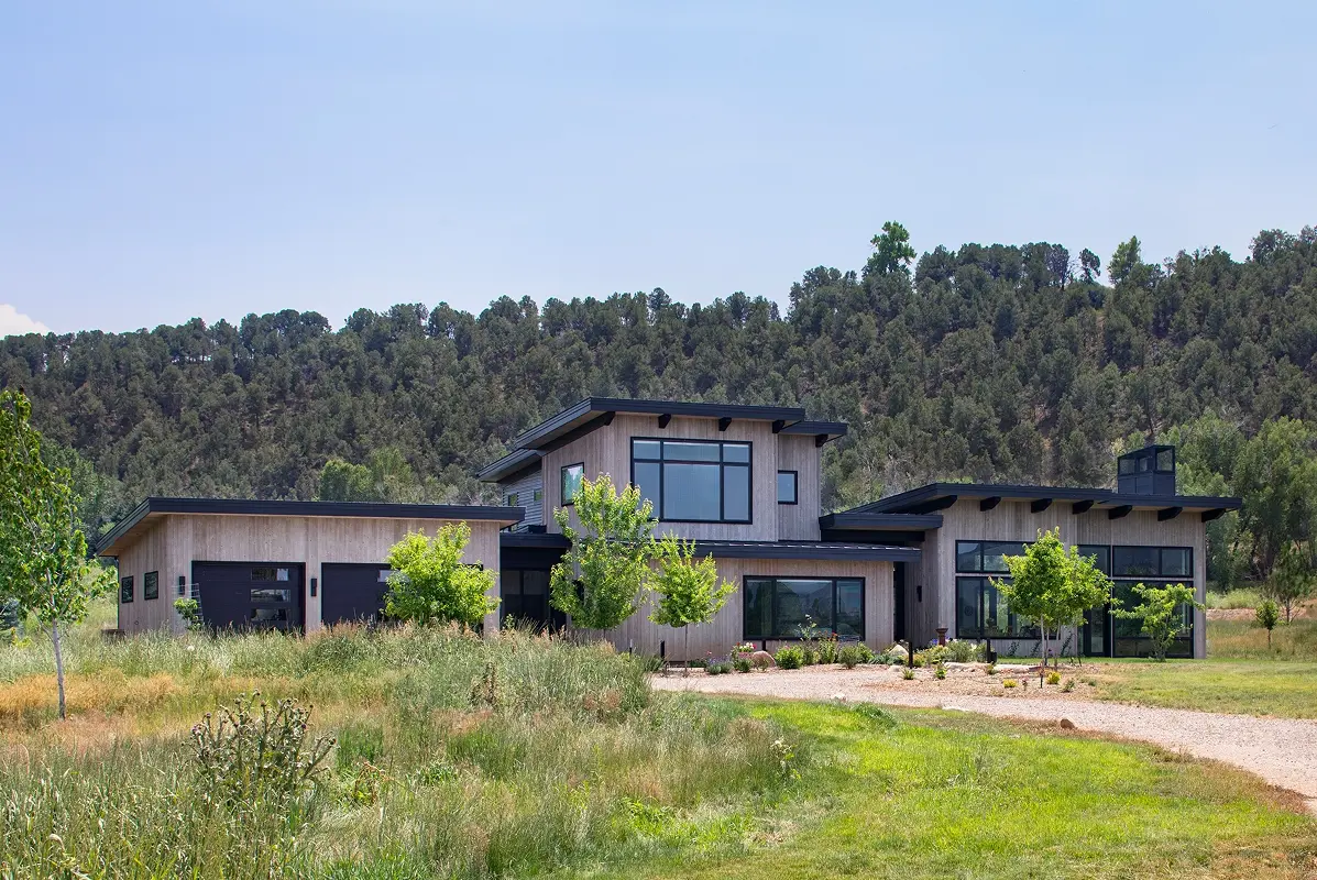 Luxury mountain home exterior with garage-facing elevation and wooded hillside backdrop.