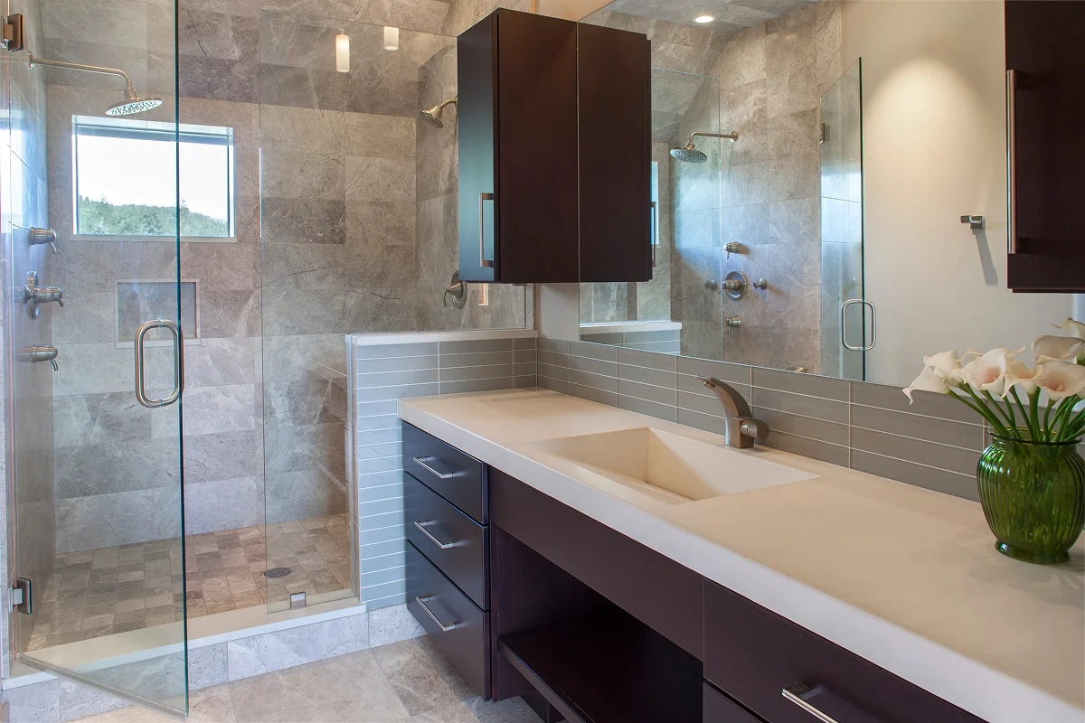 Contemporary bathroom renovation with glass walk-in shower, stone tile, and custom integrated vanity.