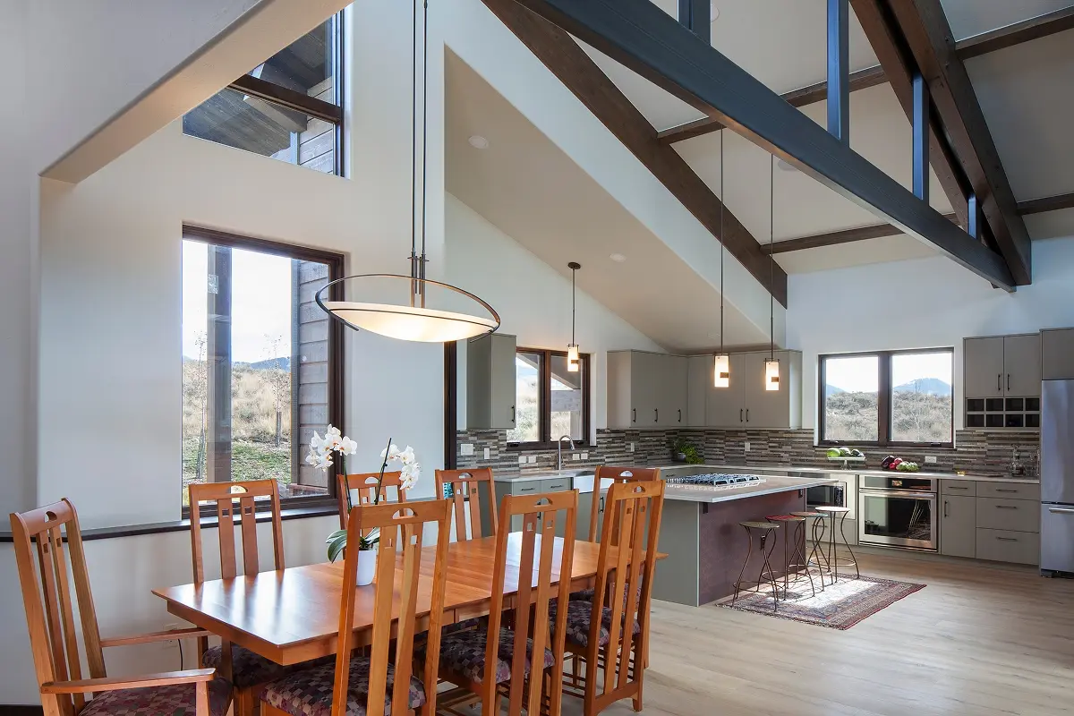 Dining area and kitchen with open floor plan, tall windows, and exposed ceiling trusses.
