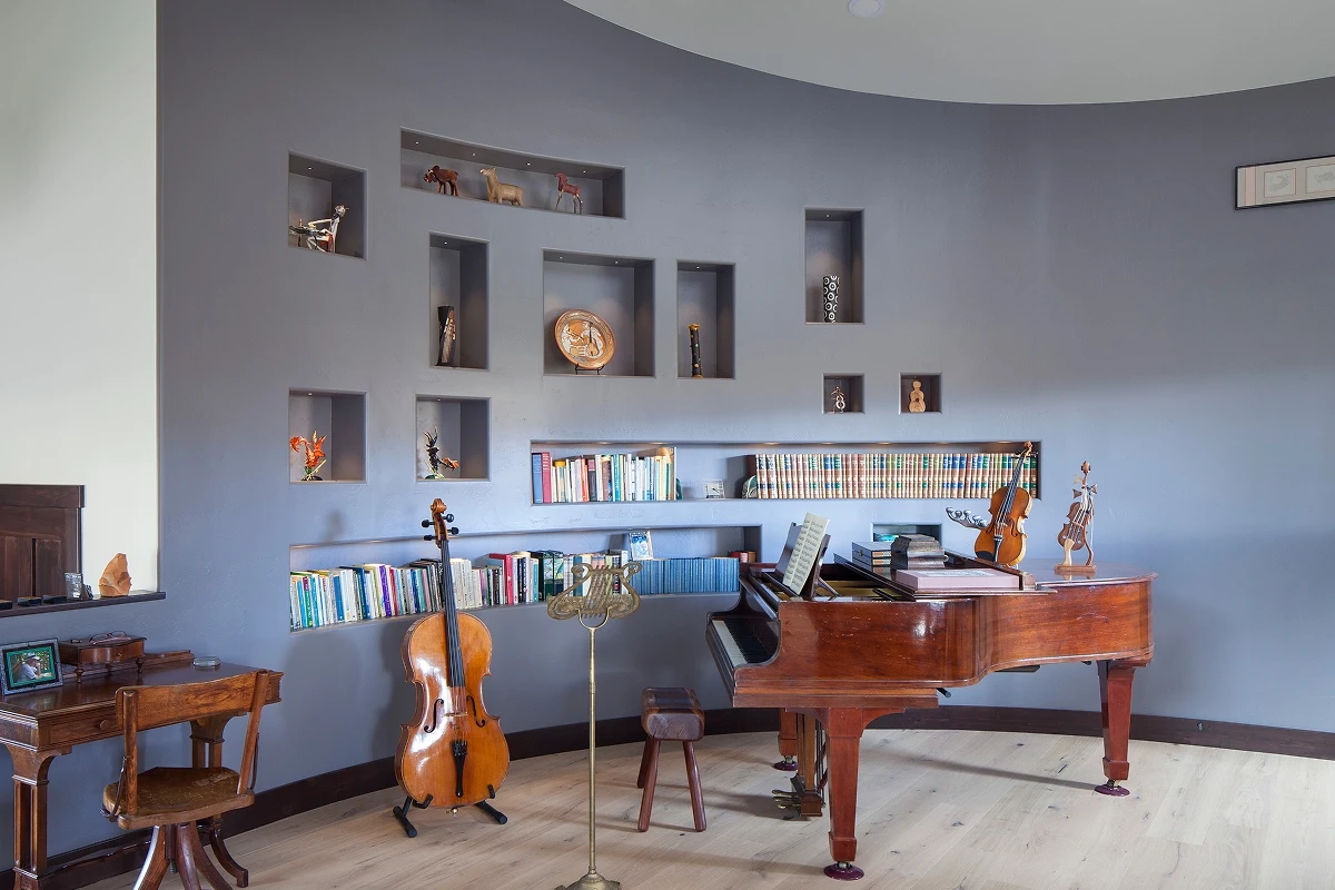 Modern music room featuring violin, cello, and piano with curved wall shelving and muted wall tones.