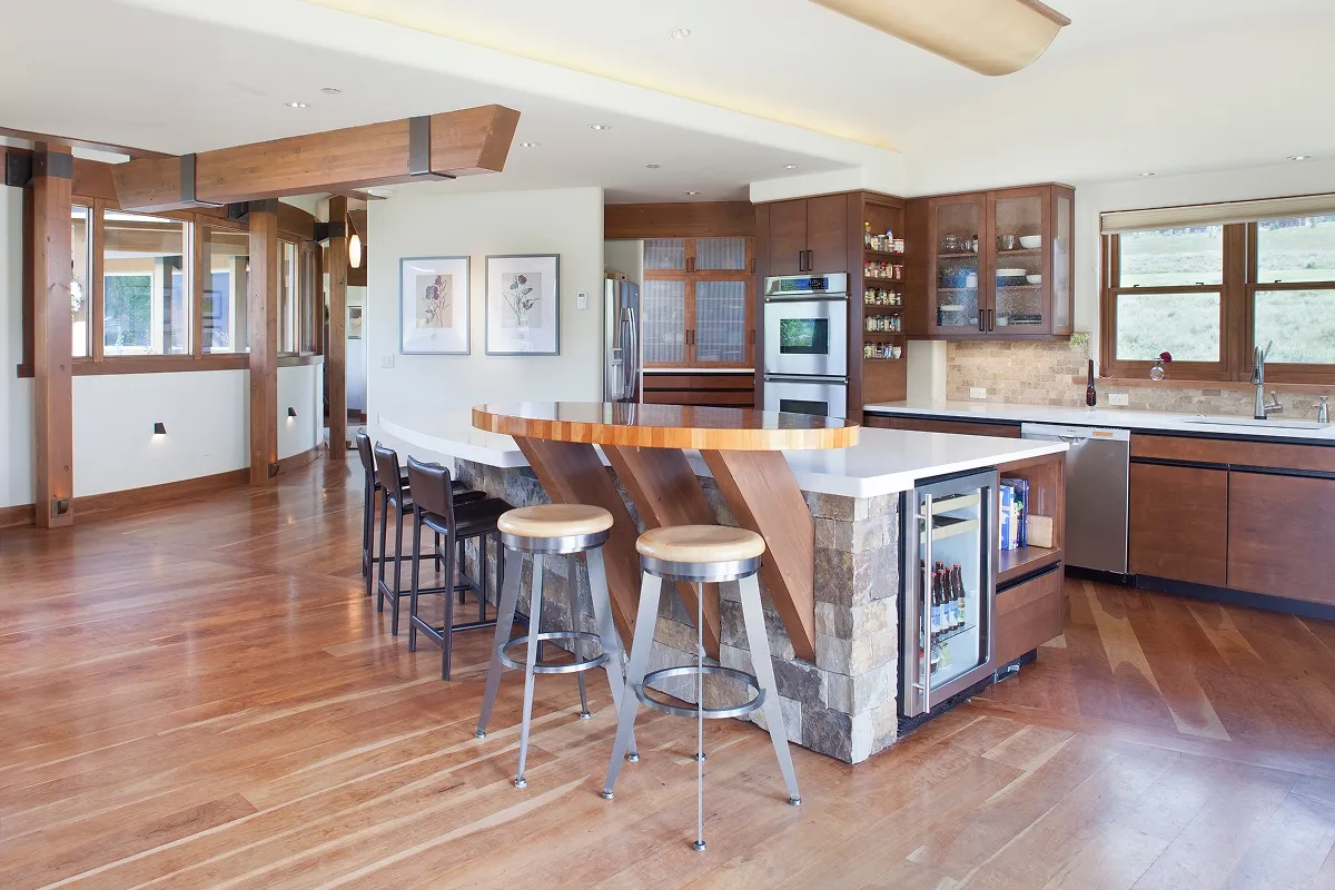 Open kitchen with curved island, cherry cabinets, built-in shelves, and stone-faced base.