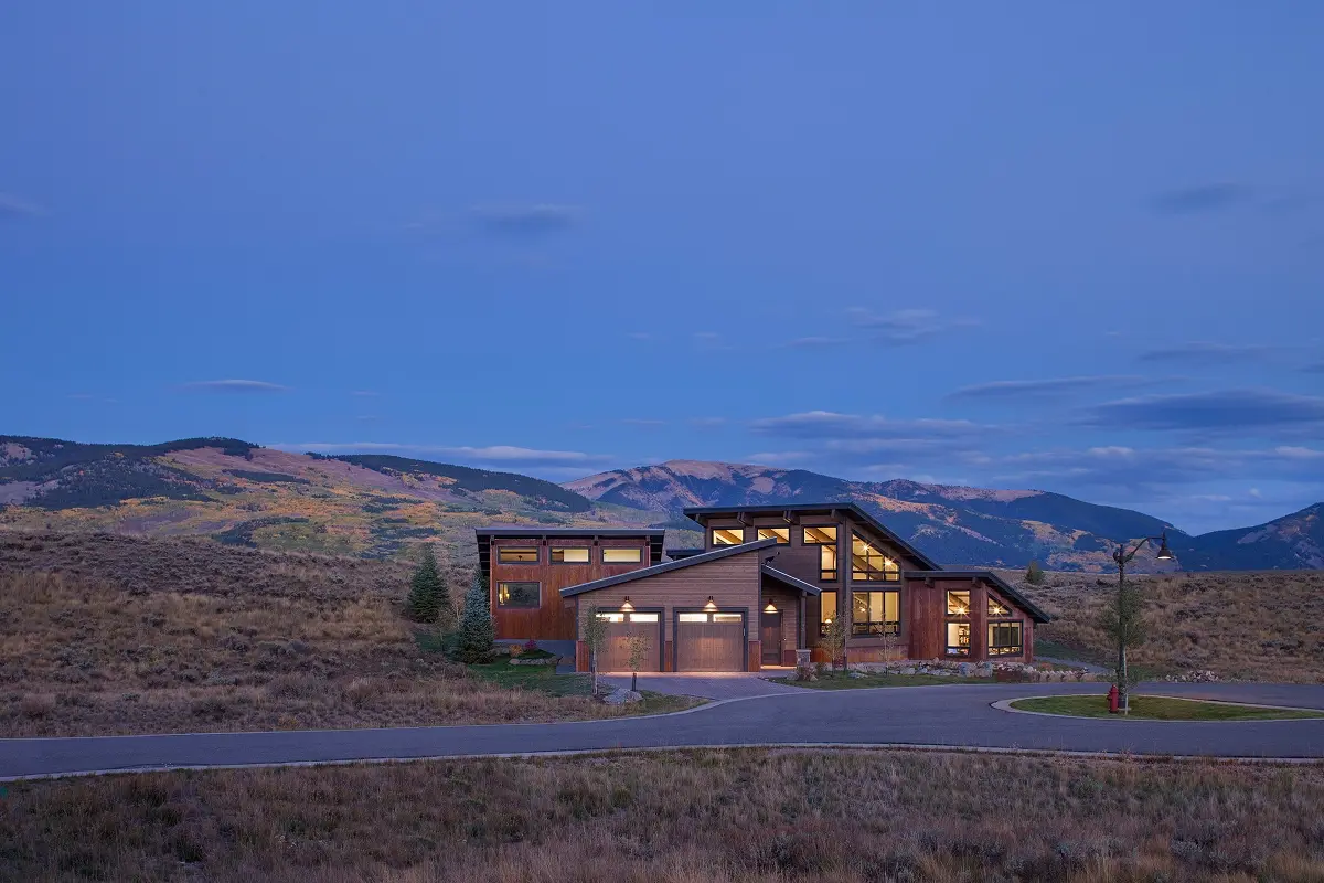 Custom Crested Butte home viewed from driveway at dusk with surrounding mountain views and warm interior lighting.