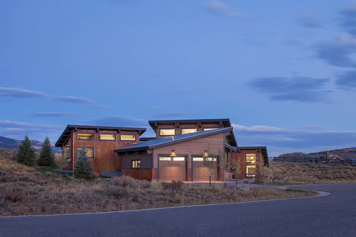 Evening view of a contemporary mountain home with low shed rooflines and glowing interior lights.