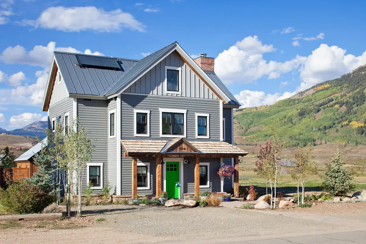 Covered front porch with timber columns and green door framed by native plantings and stonework.