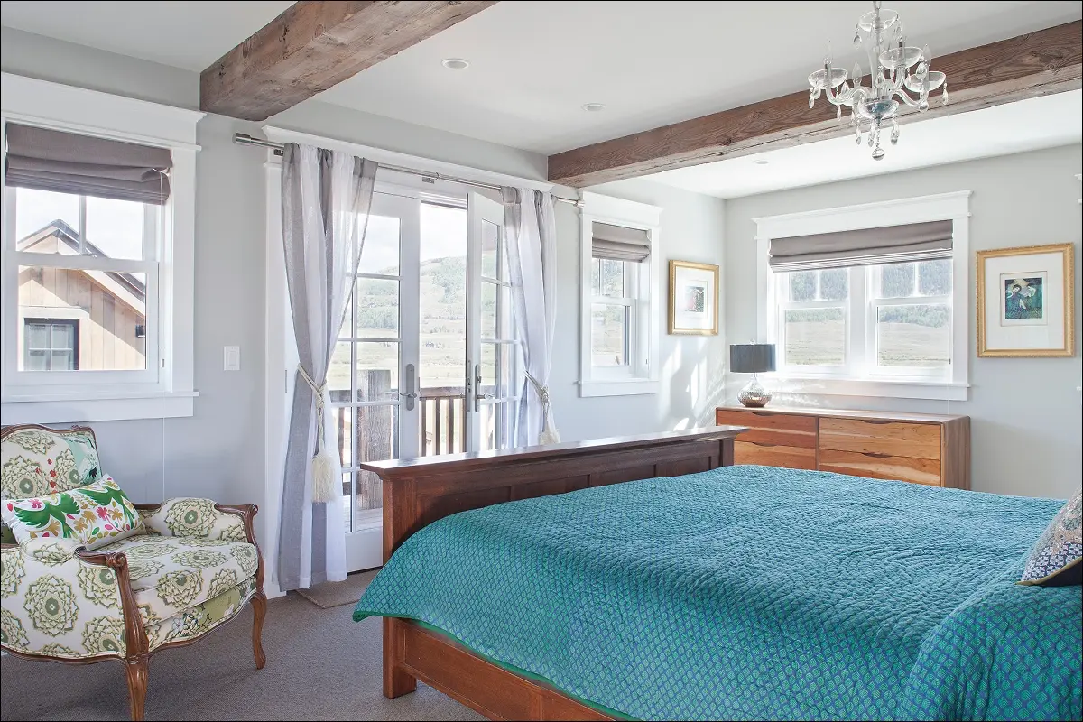 Primary bedroom with wood bed frame, chandelier, and large windows overlooking Crested Butte landscape.