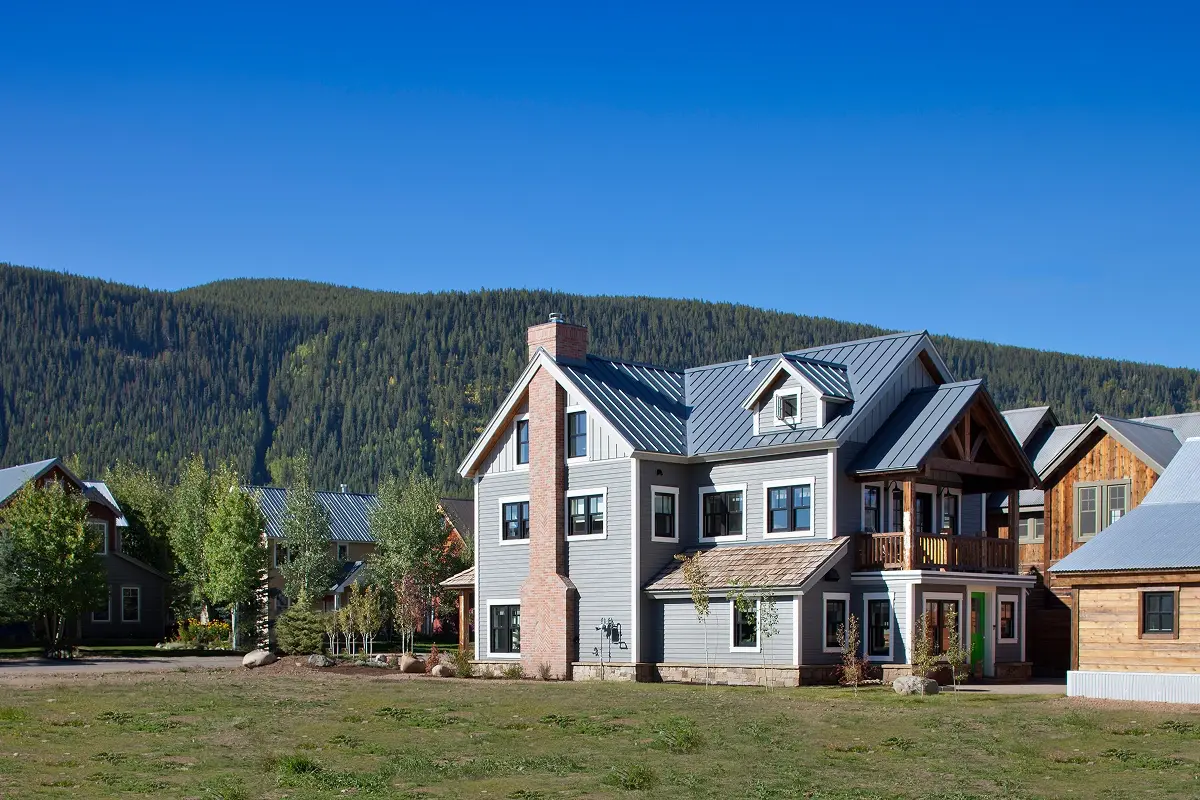 Side view of mountain home with classic chimney and gable rooflines against forested hillside.