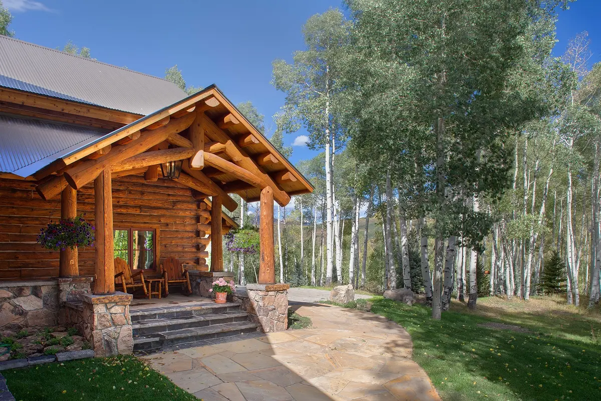 Covered log porch with timber columns and stone base, surrounded by aspens near Crested Butte.