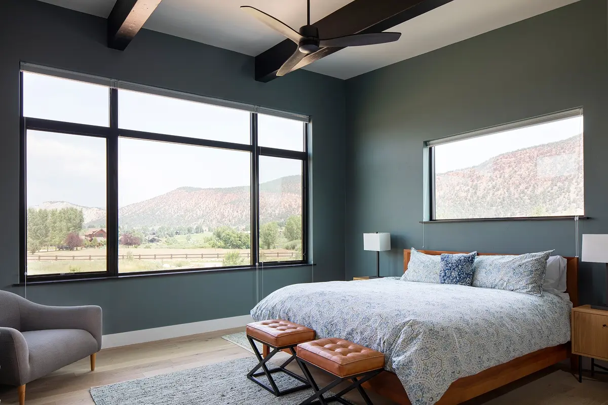 Primary bedroom in mountain home with panoramic views framed by large modern windows.