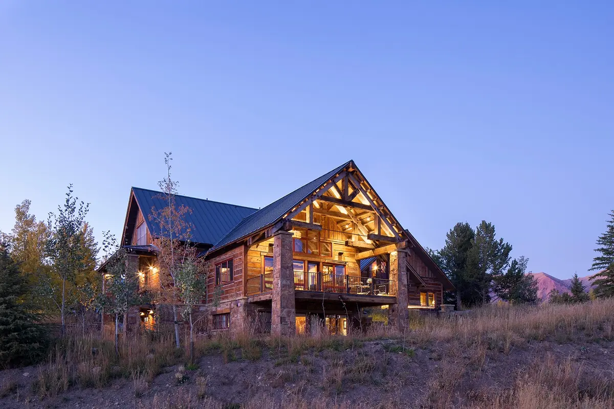 Evening view of mountain lodge with illuminated log beams and natural wood siding.