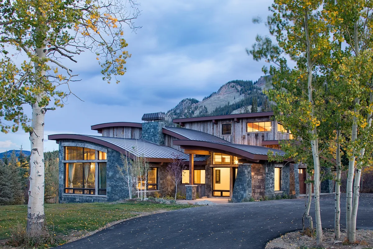 Front elevation of Surround House framed by aspens with curved metal roof and dramatic mountain backdrop.