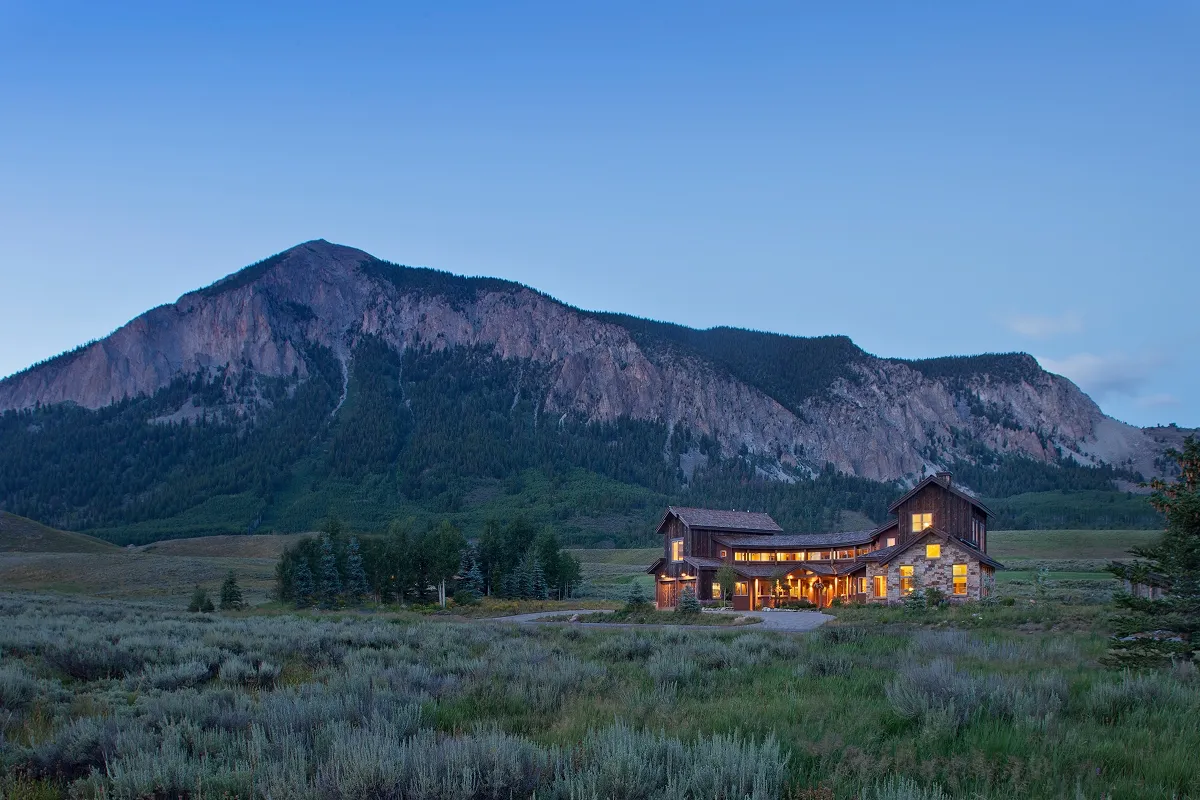 Wide-angle twilight view of a mountain modern home nestled in the Slate River Valley with mountain backdrop.