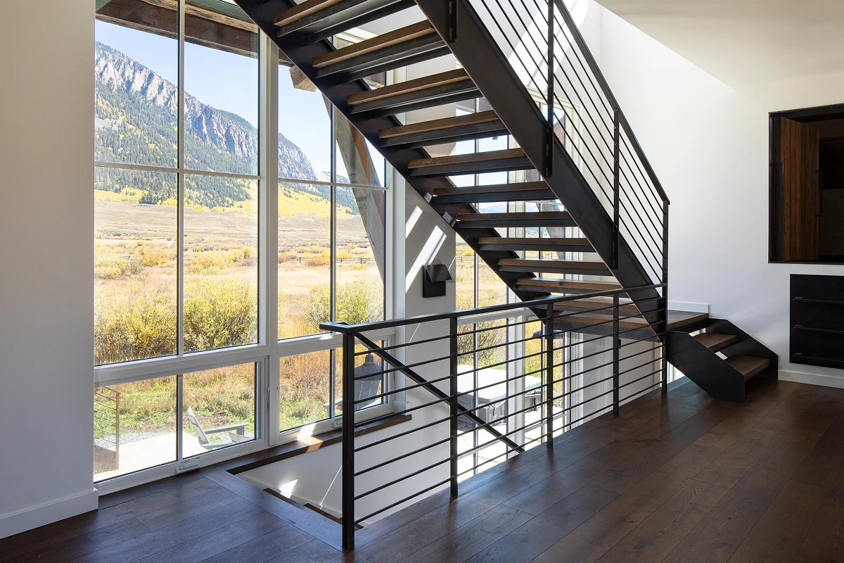 Floating staircase with metal railings set against full-height glass offering Rocky Mountain views.