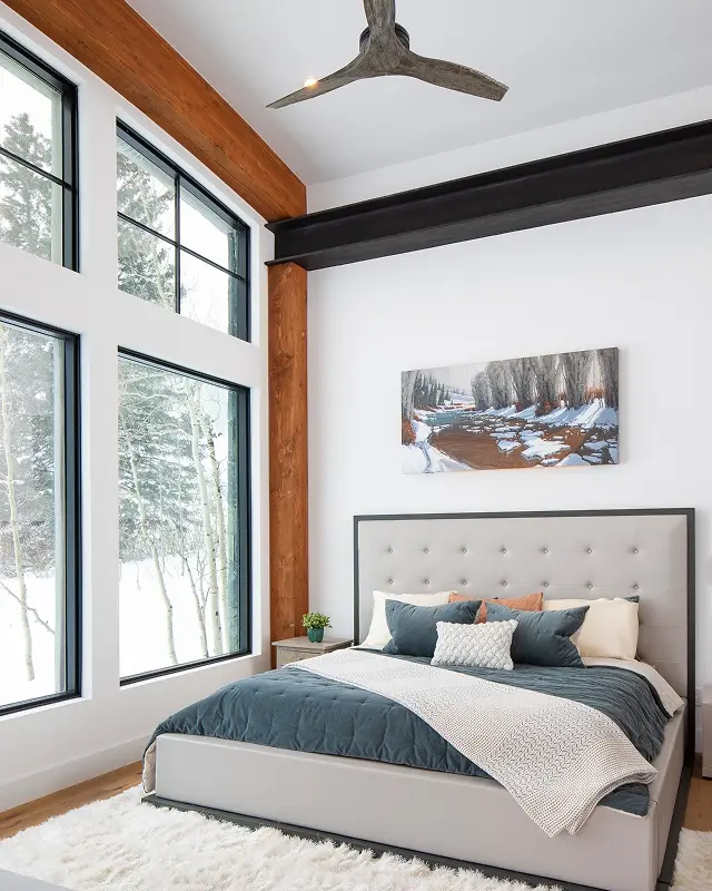 Contemporary bedroom with large picture windows, wood accents, and snowy forest views in Crested Butte, Colorado.