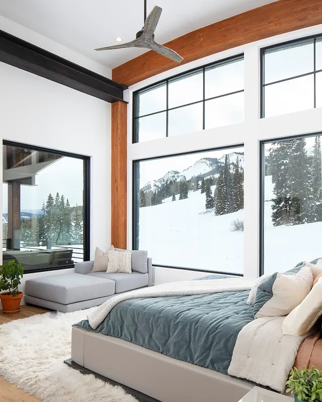 Primary bedroom with panoramic windows, vaulted wood beams, and snowy mountain views in a modern Crested Butte home.